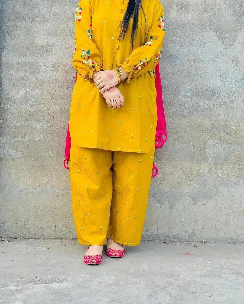 Person wearing a yellow traditional outfit with floral patterns against a gray wall.