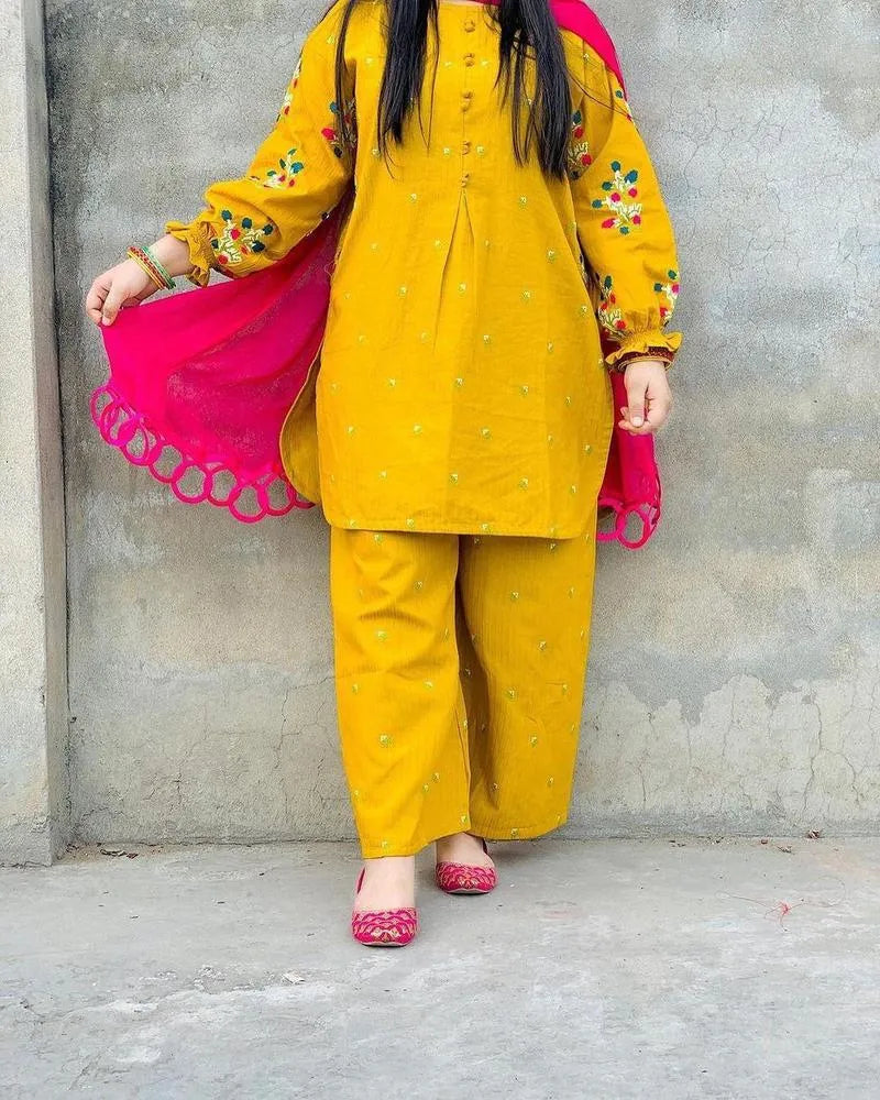 Person wearing a yellow traditional outfit with pink dupatta against a gray wall.