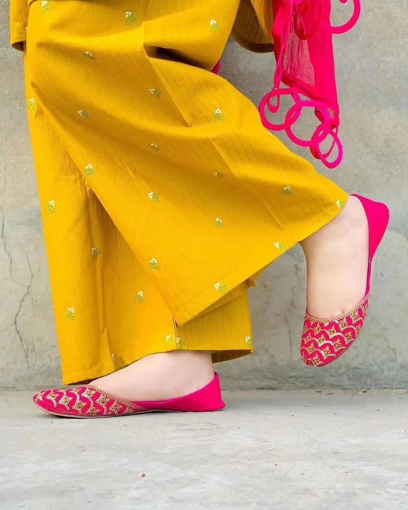 Person wearing yellow traditional outfit with pink shoes on a plain background