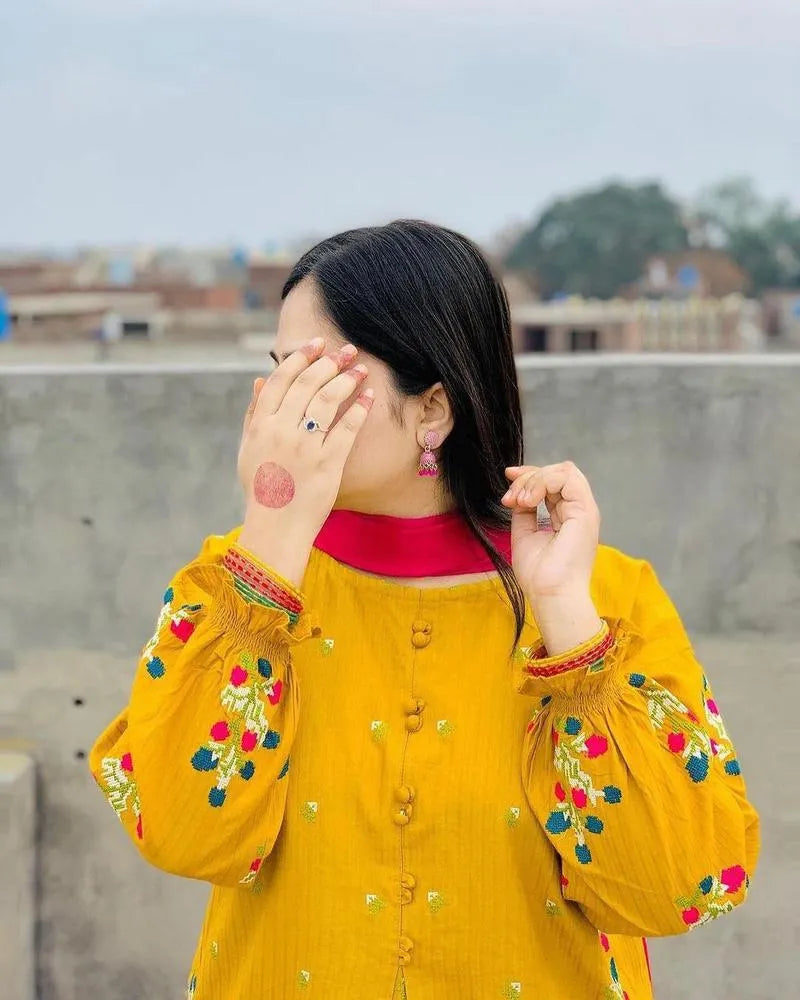 Person wearing a yellow embroidered outfit with a red inner collar, standing outdoors.