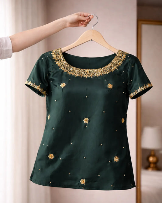 Green blouse with gold embroidery on a hanger against a neutral background