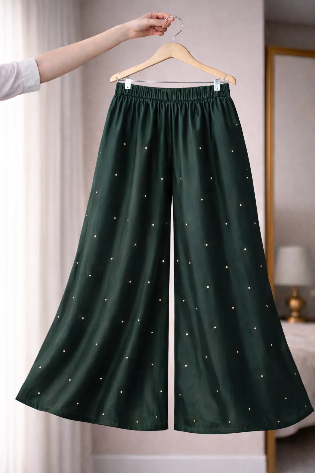 Green pants with star patterns on a hanger against a neutral background