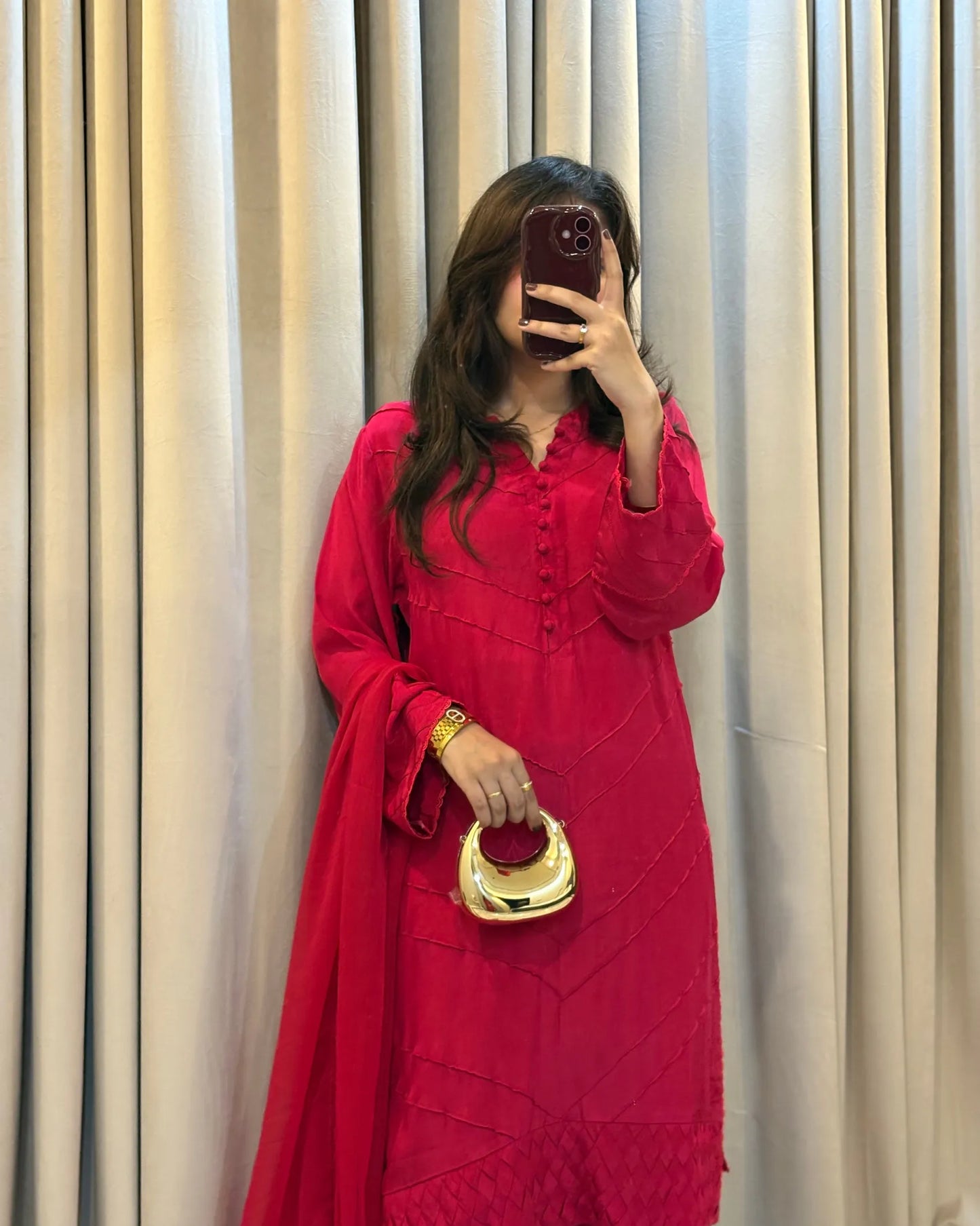 Person wearing a red outfit with a gold handbag in front of beige curtains
