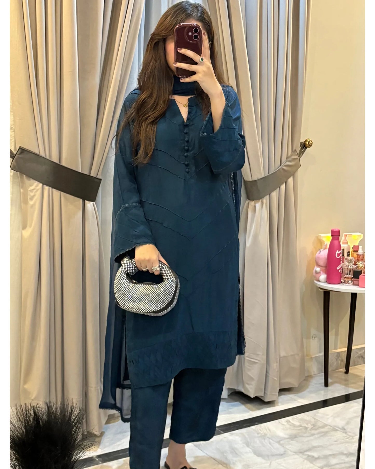 Person wearing a teal outfit with a matching handbag in front of beige curtains.