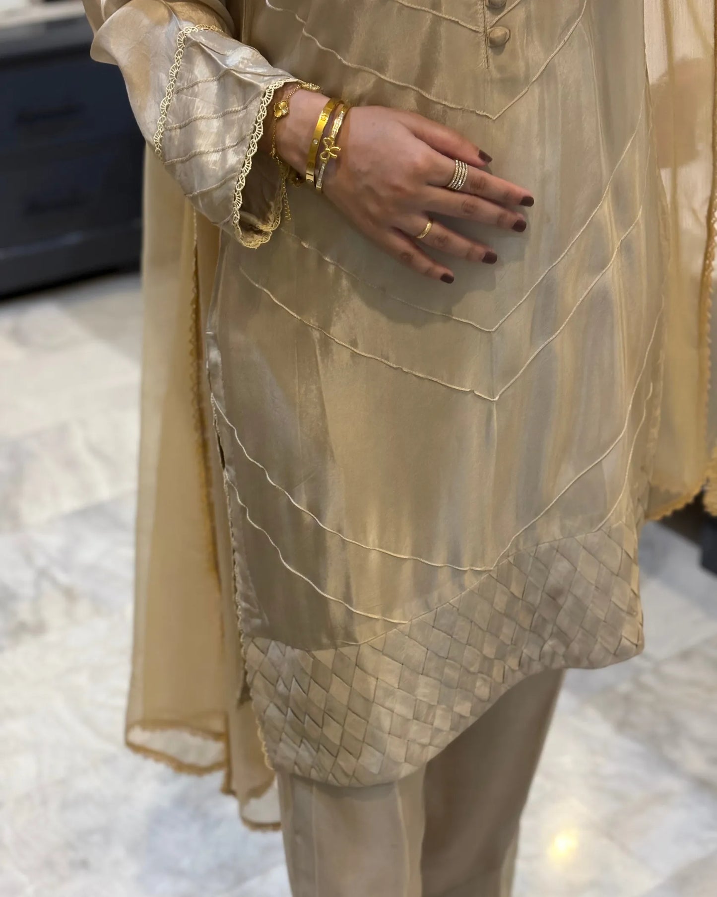 Person wearing a beige traditional outfit with intricate patterns on a light background