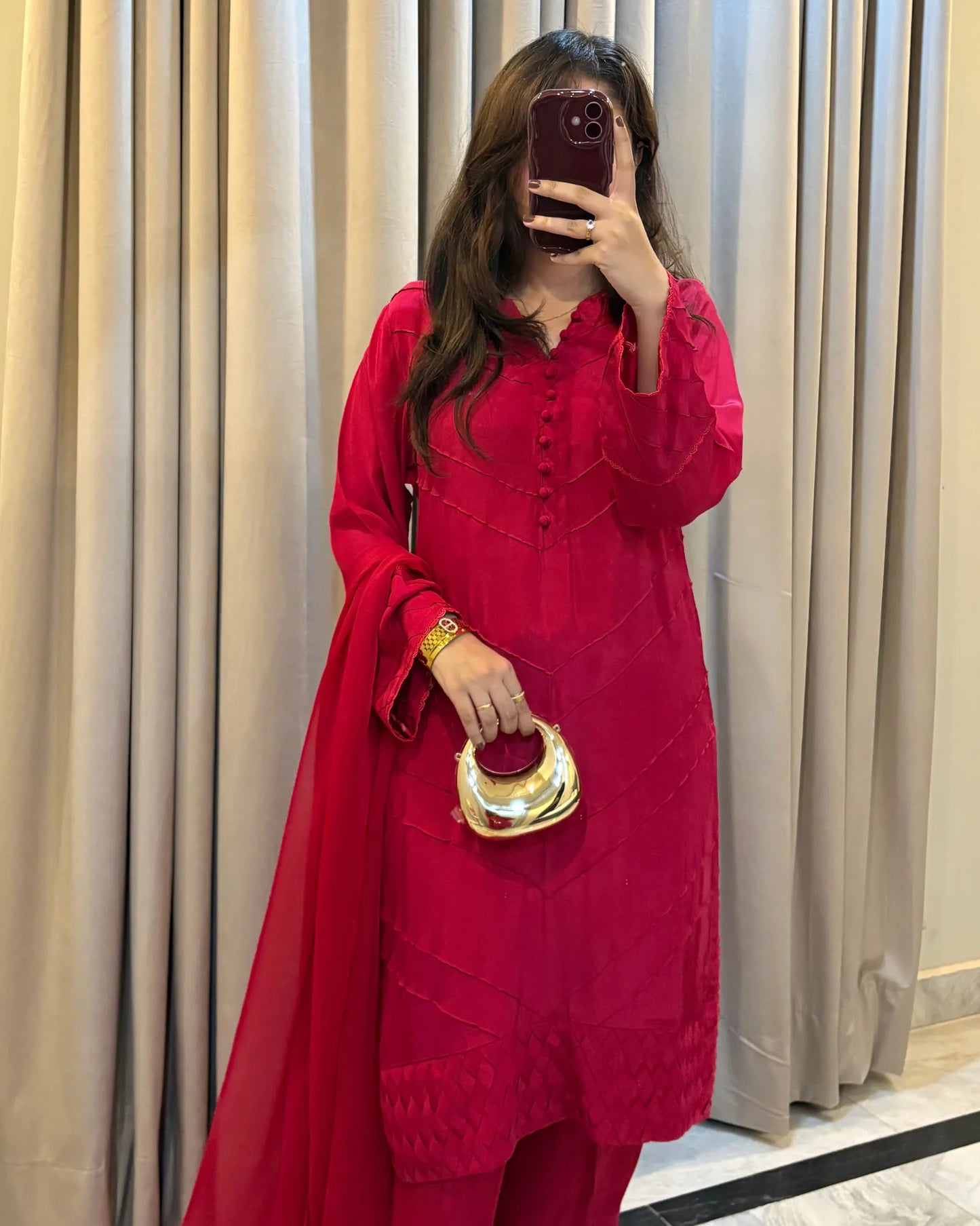 Person wearing a red outfit with a gold clutch in front of beige curtains