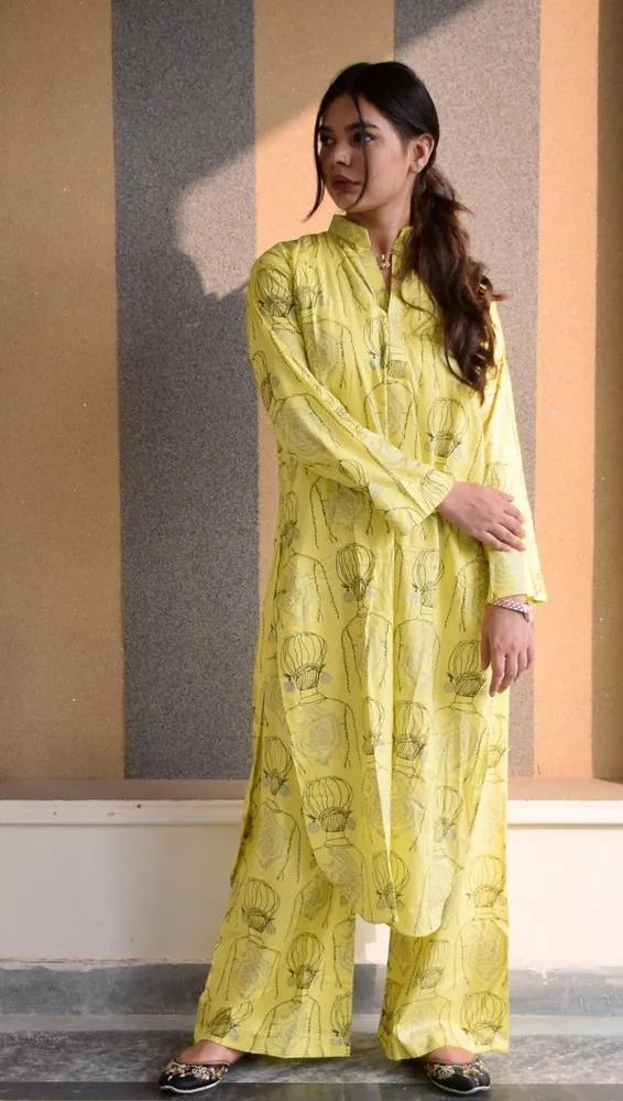 Woman wearing a yellow traditional outfit with intricate patterns, standing against a neutral background.