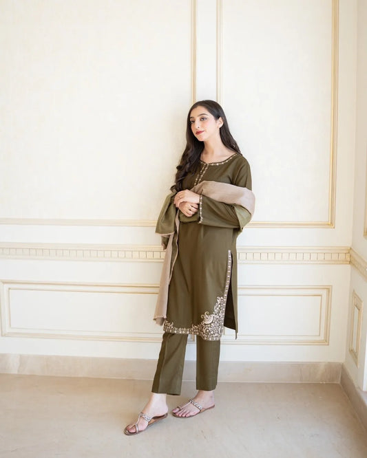 Woman in an olive green traditional outfit with a beige scarf against a white wall.