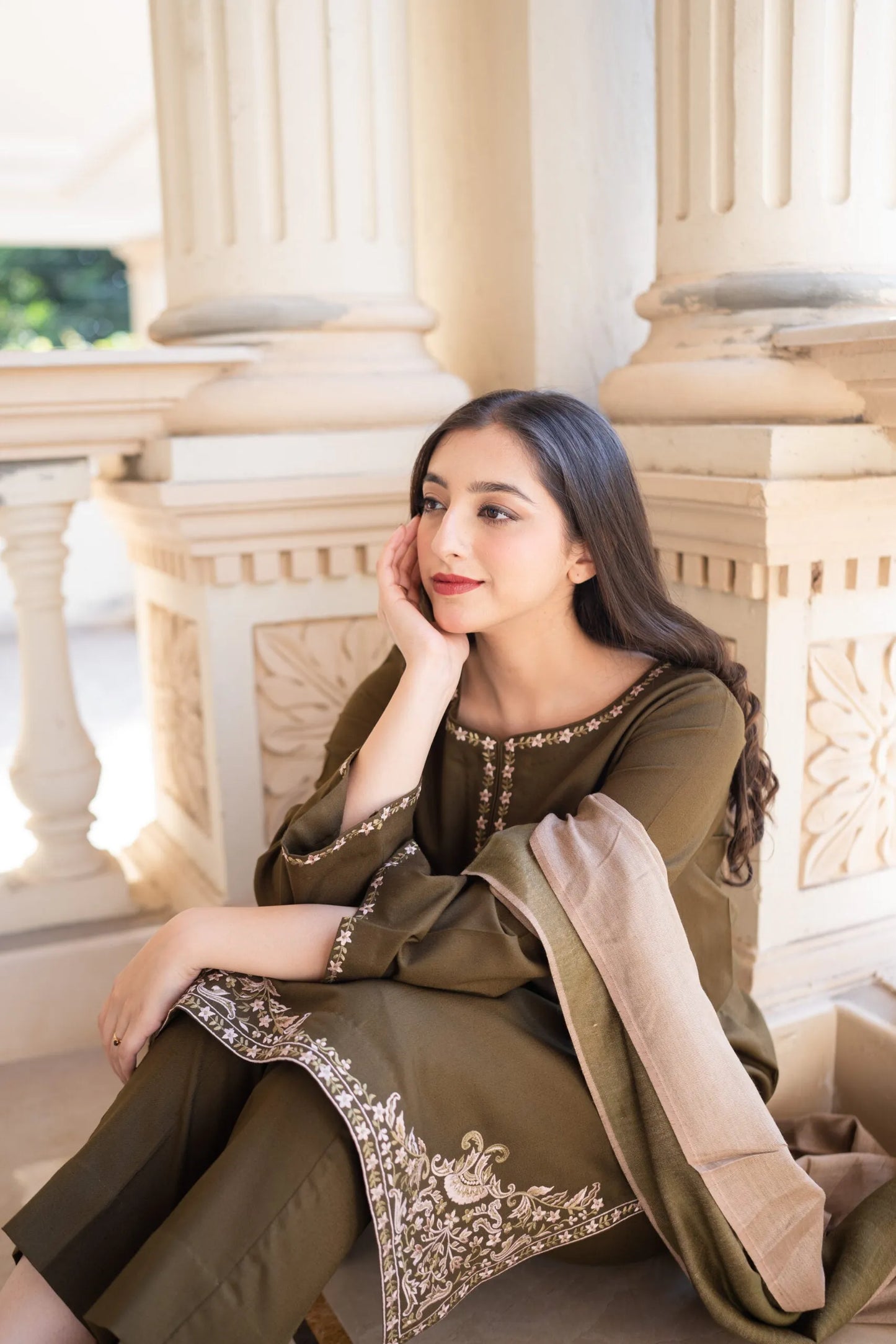 Woman in traditional outfit sitting against classical architecture