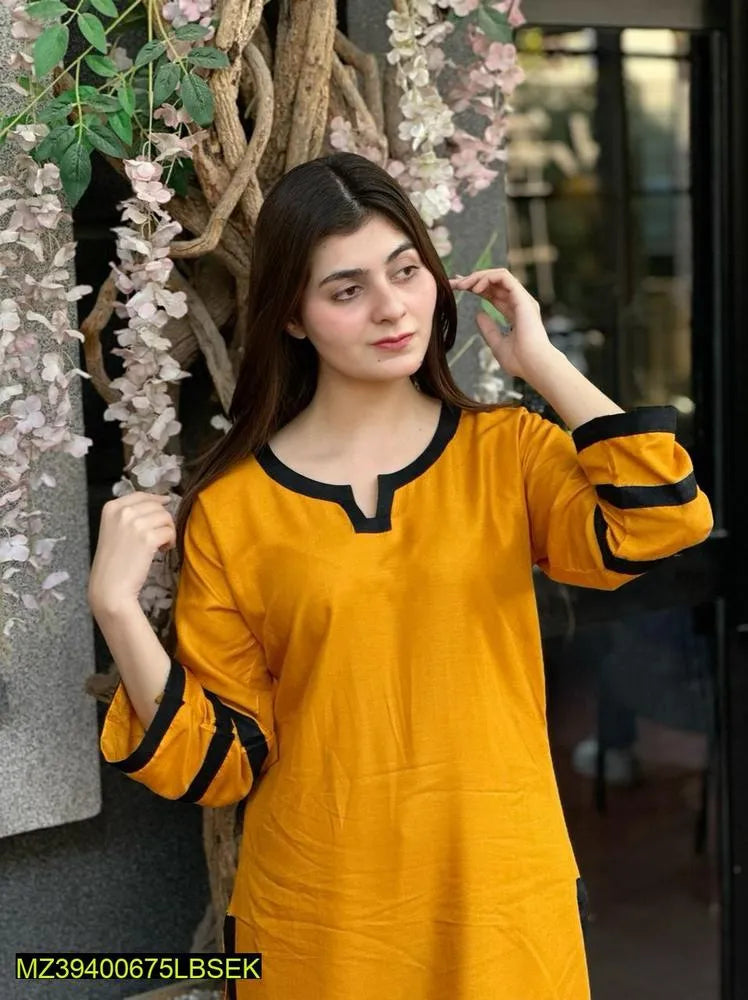 Woman wearing a yellow kurta with black accents in an indoor setting with decorative elements.